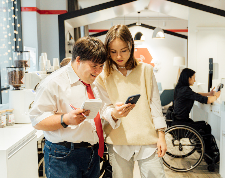 A man with Downs Syndrome smiling while working at a cafe with his coworker.