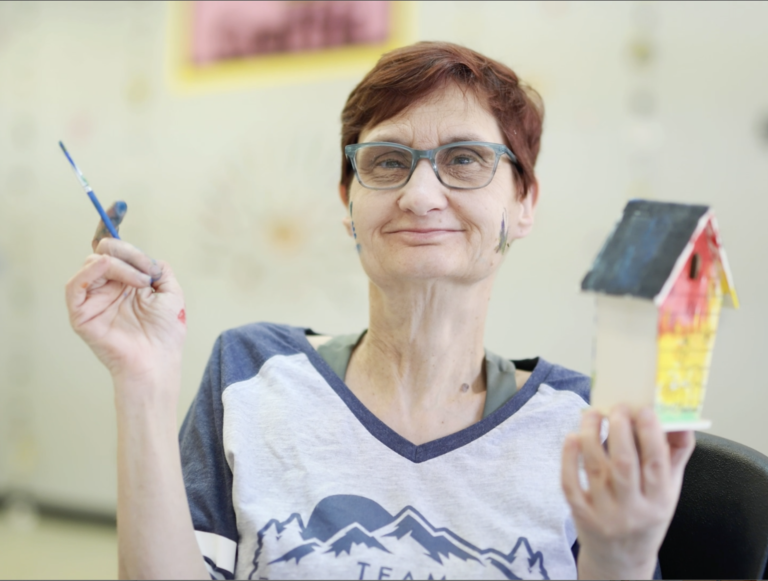 A female CPLF client holding painting supplies and smiling.